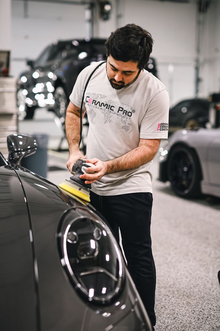 our-story-02 A man carefully polishes a sleek sports car in a professional auto detailing garage.