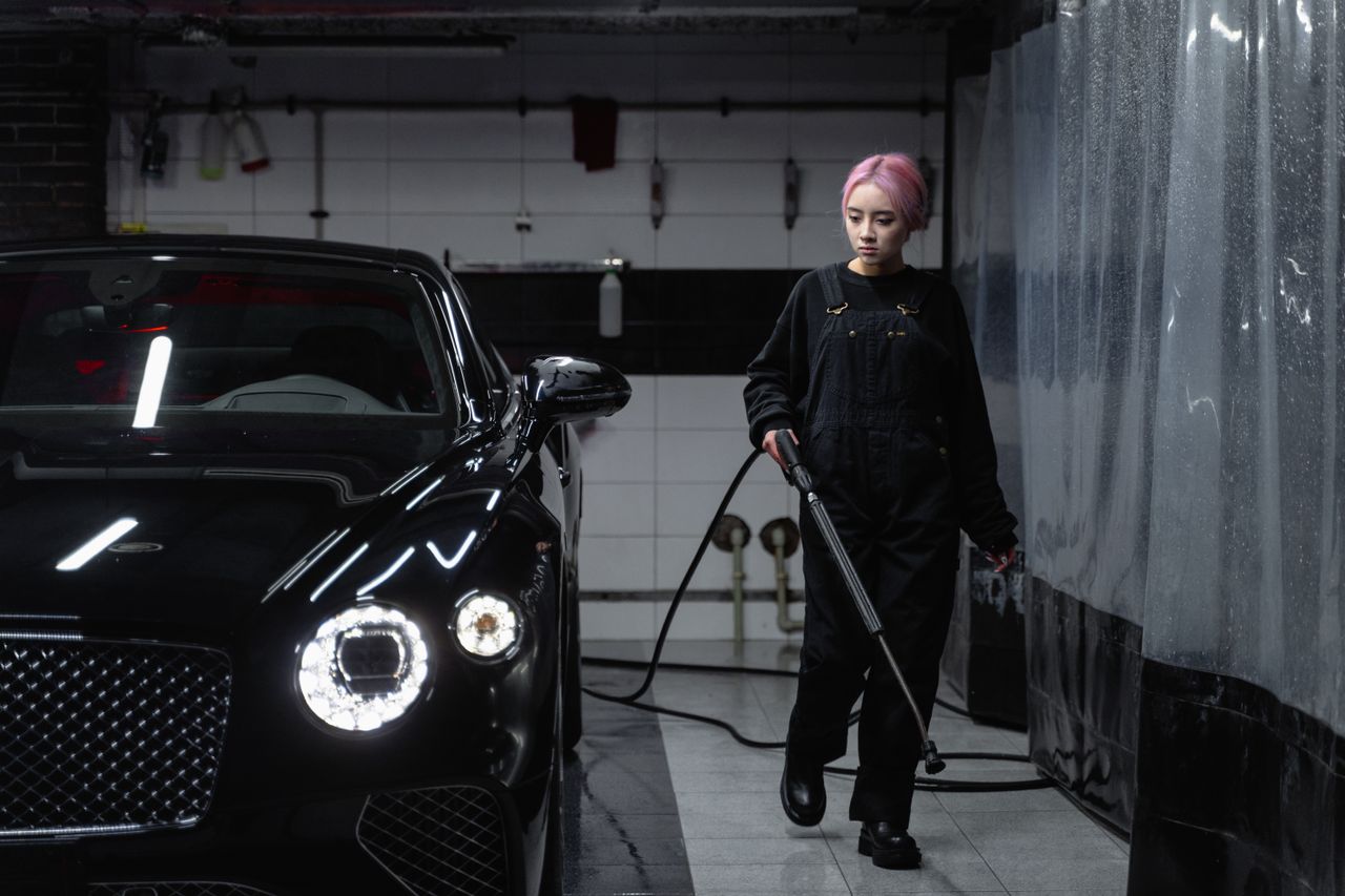 our-mission-01 Woman cleaning luxury black car at car wash garage using hosepipe.